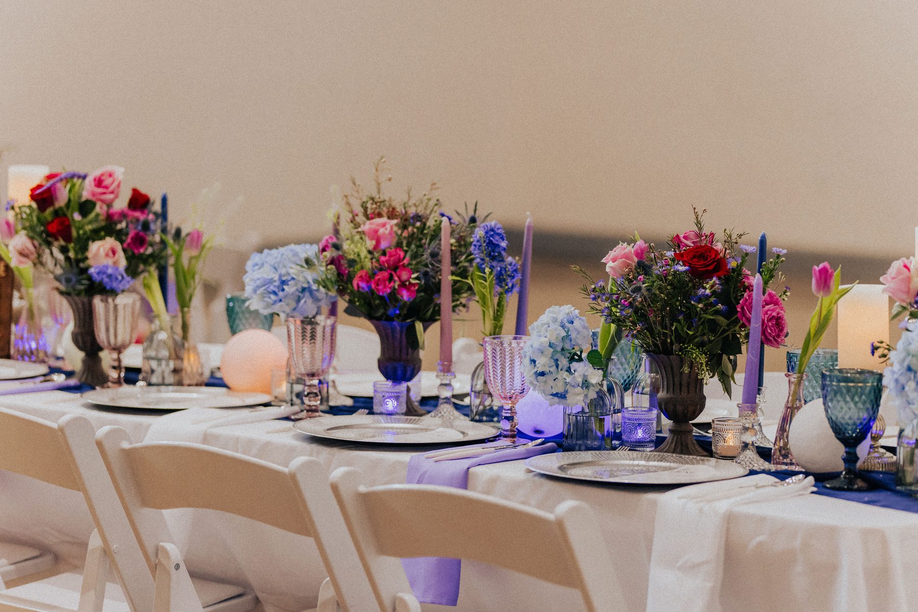 Long reception table styled with jewel-tone florals and candlelight