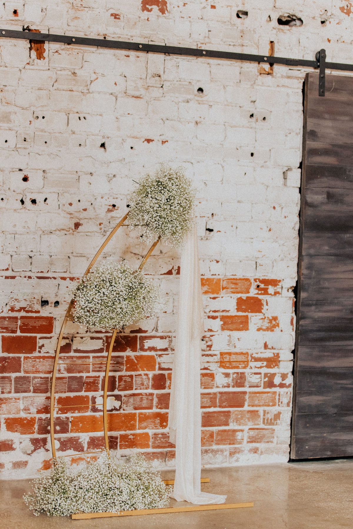 Gold arch with baby's breath and flowing drape against an exposed brick wall
