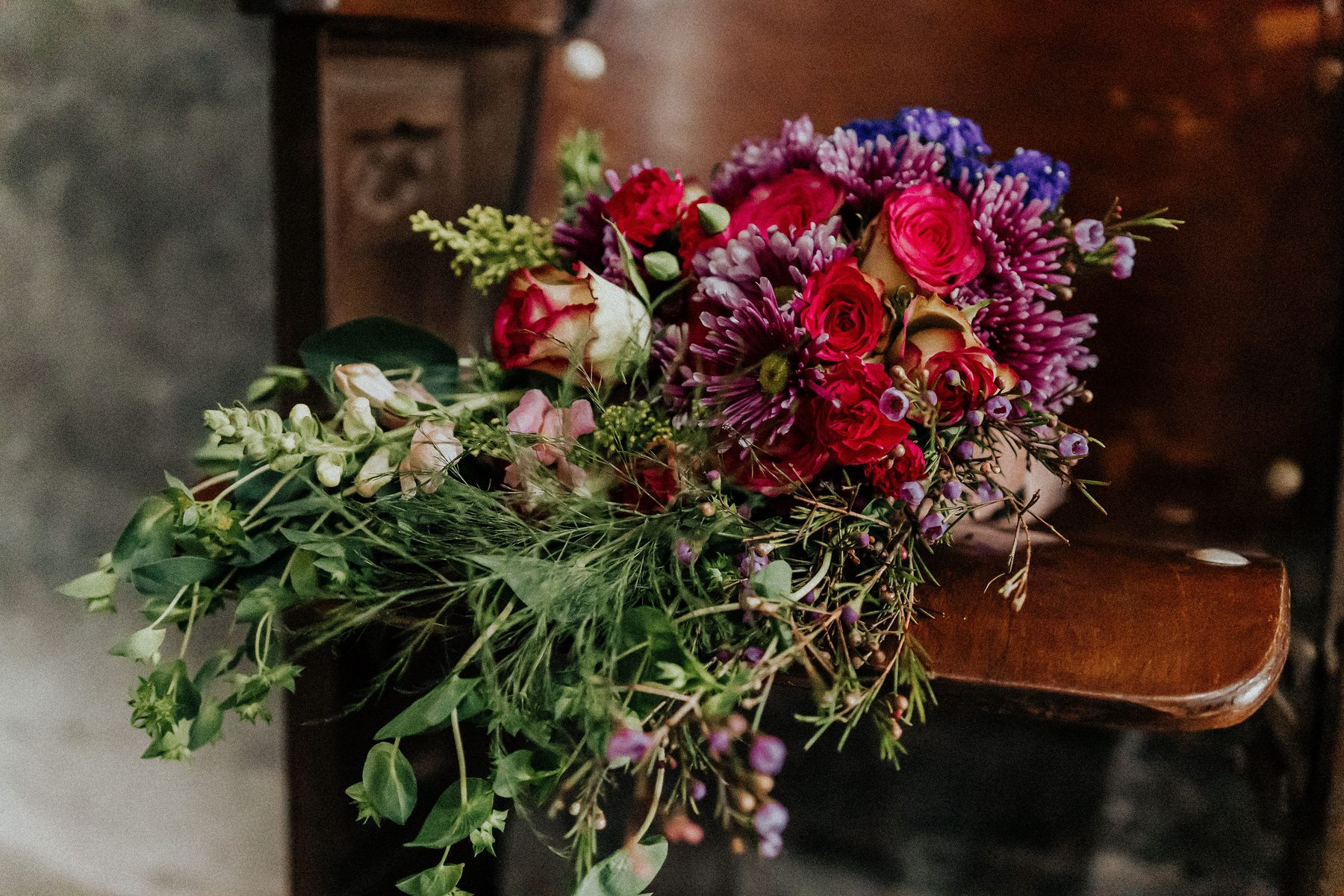 Jewel-toned bridal bouquet of red and pink roses with purple accents