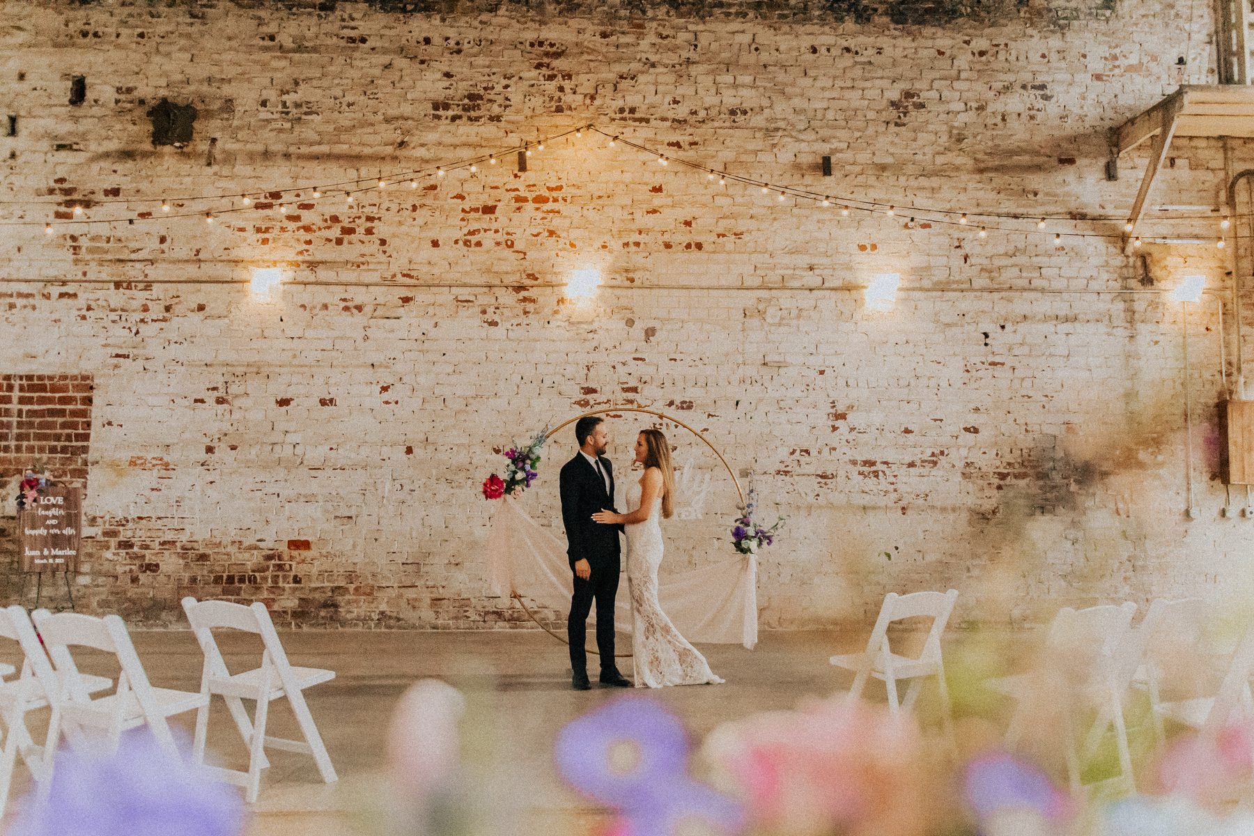 Couple at a modern circular arch with string lights against exposed brick
